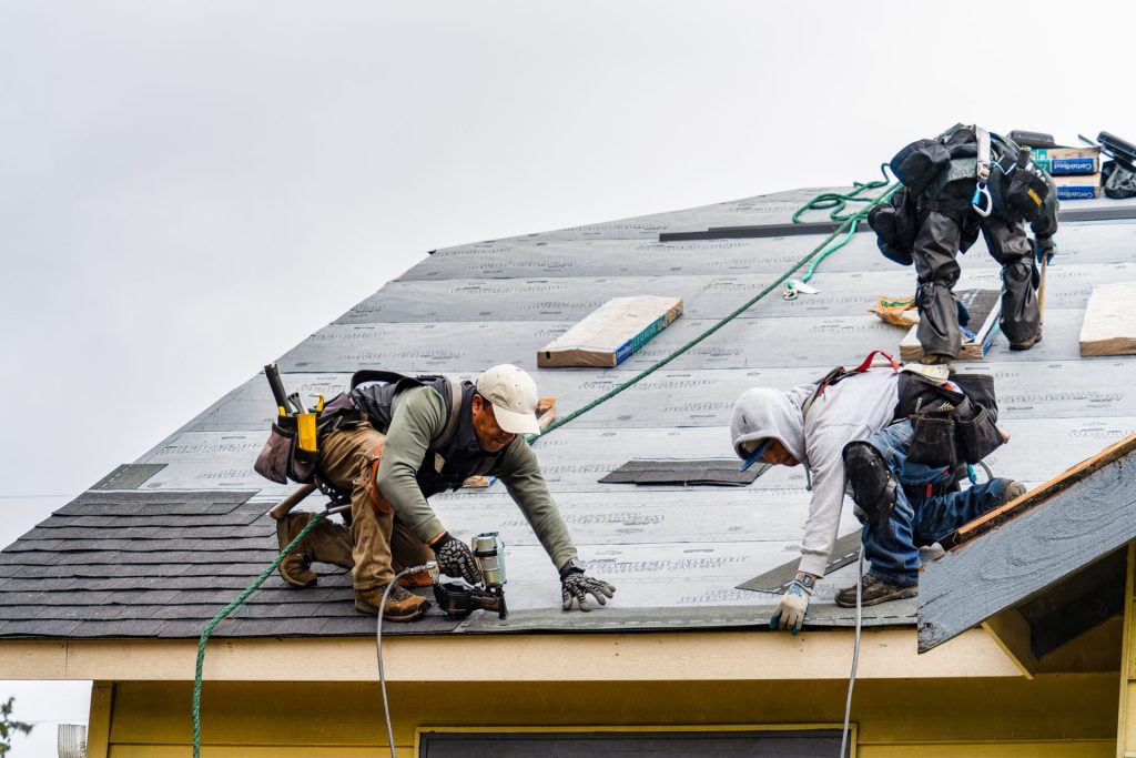 Three people using tools to attach shingles to a roof.