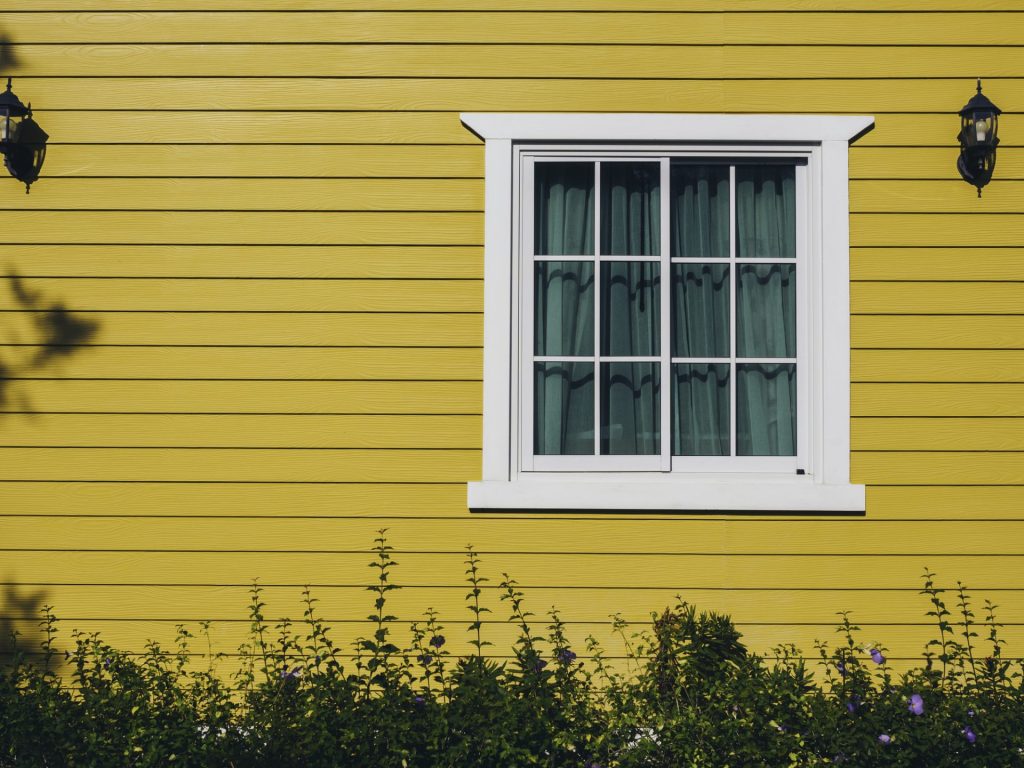 A wall with yellow siding and a white window