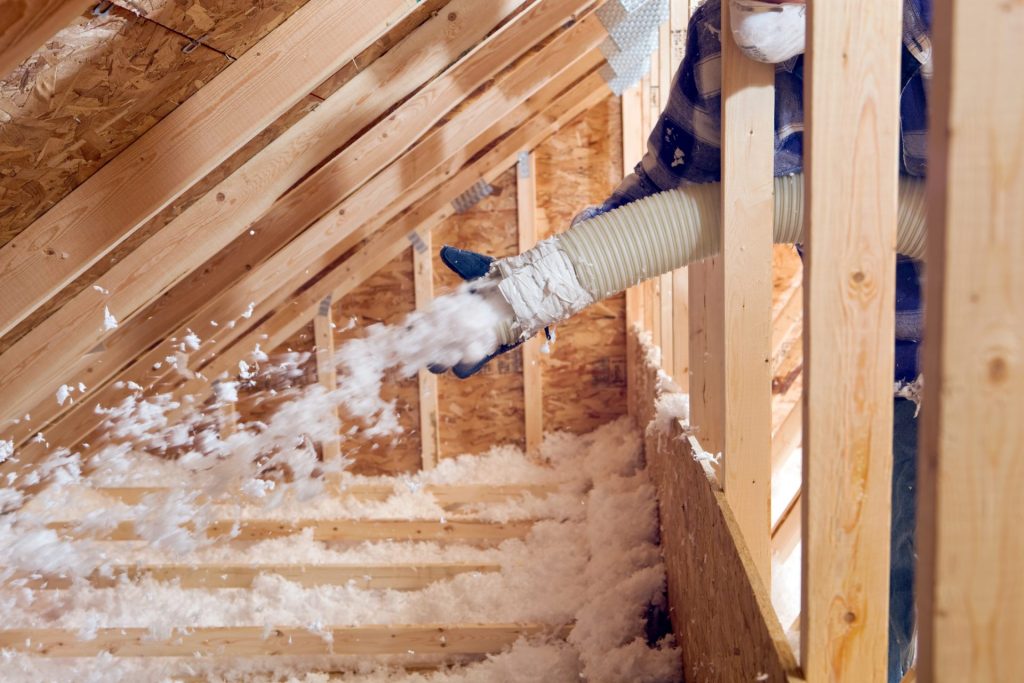 A person installing blown in attic insulation with a large tube.